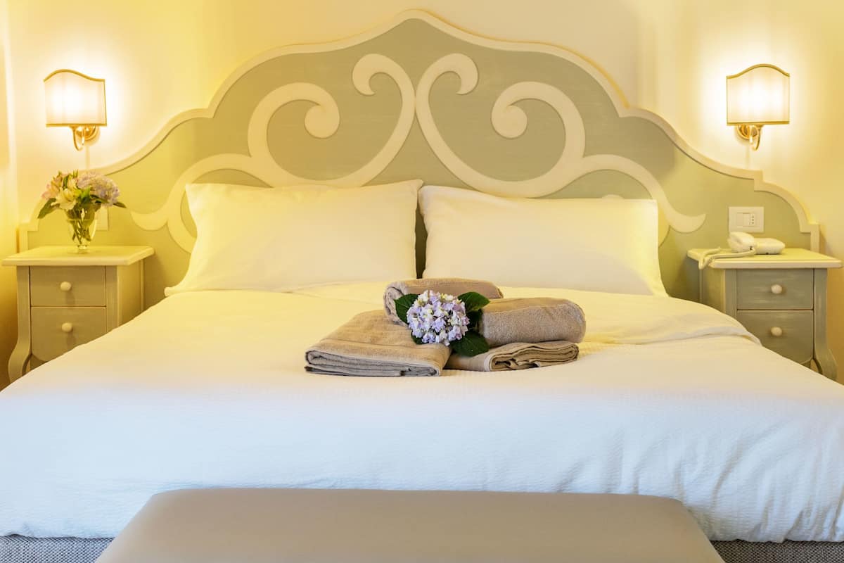 A neatly made bed with white linens, two bedside tables with lamps, and a vase with flowers on one table.