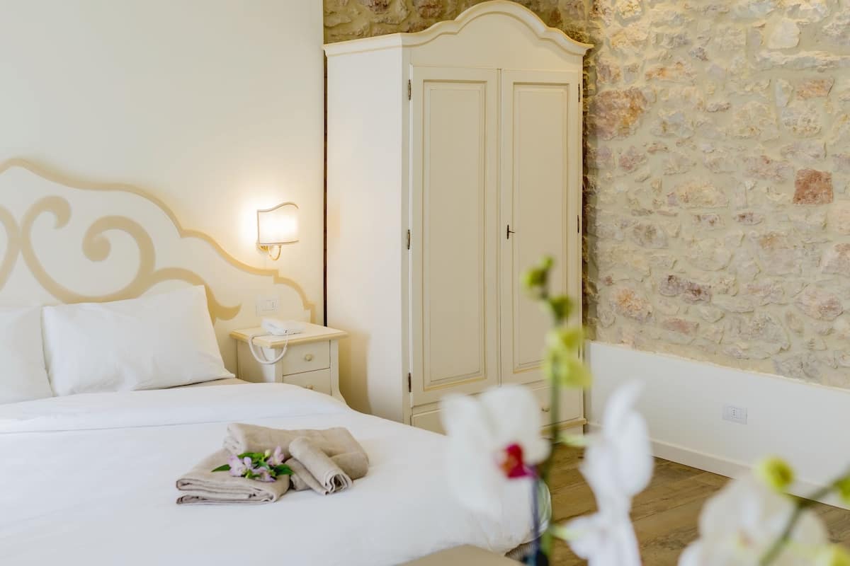 A hotel room with a bed, white wardrobe, and a stone wall.