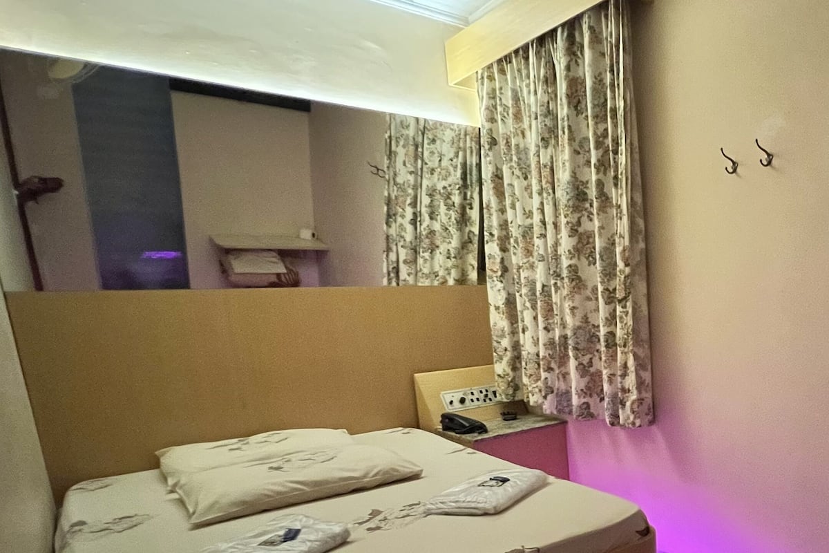 A modern hotel room with a large bed, a nightstand, a lamp, and a window with floral curtains.