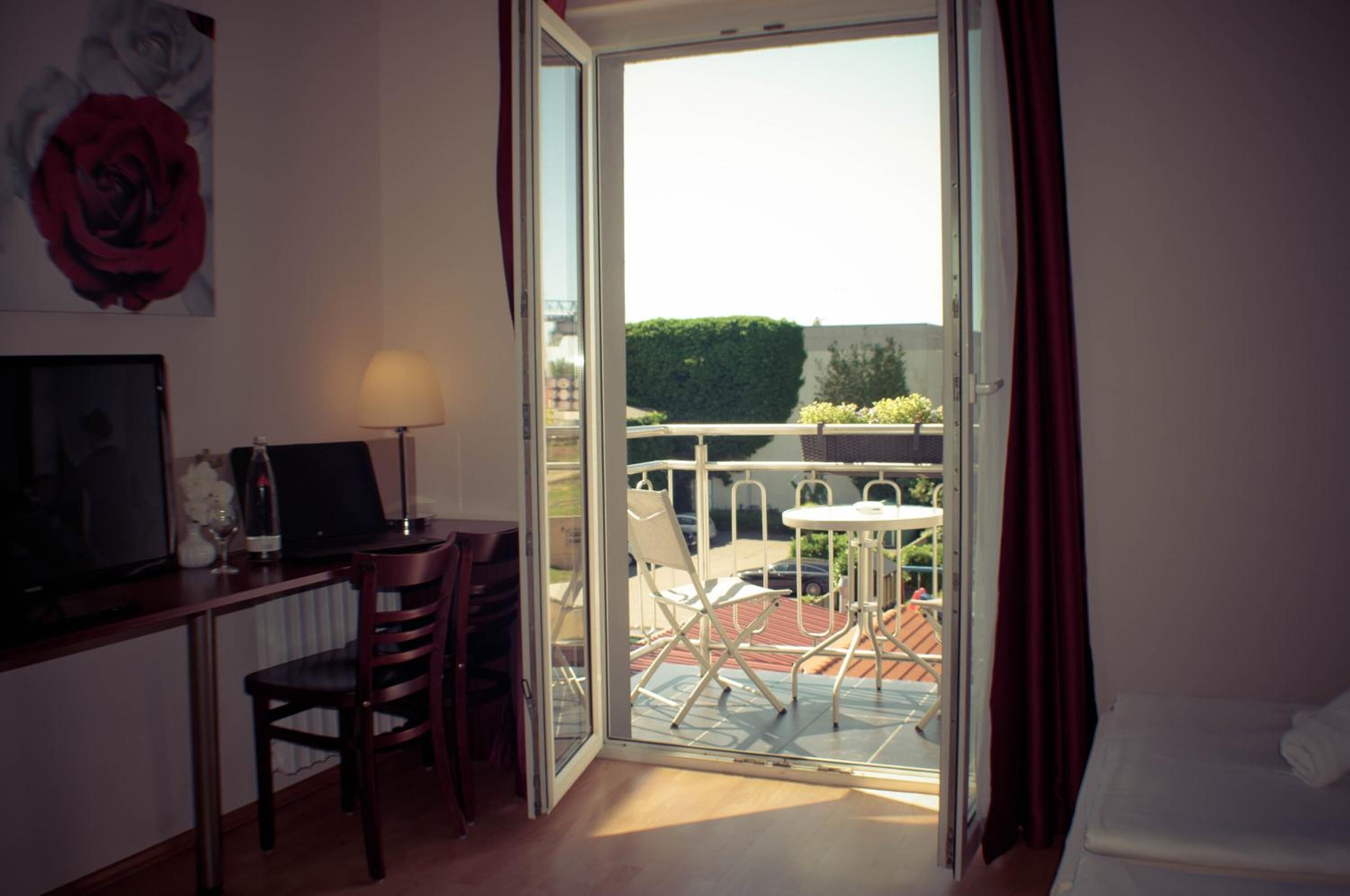 A room with a desk, chair, and a table with chairs outside on a balcony.