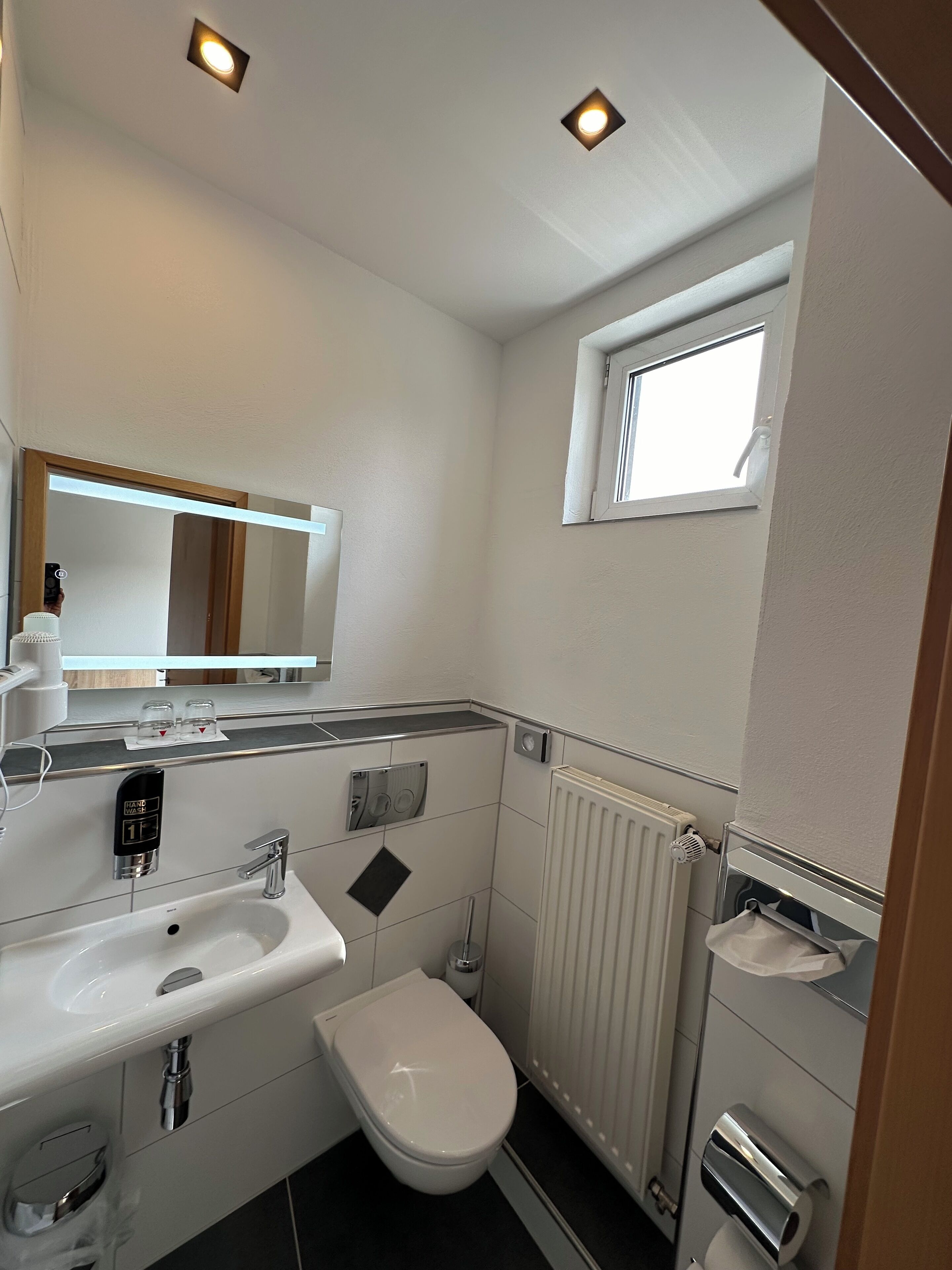 Un baño pequeño con lavamanos blanco, inodoro, espejo y ventana.