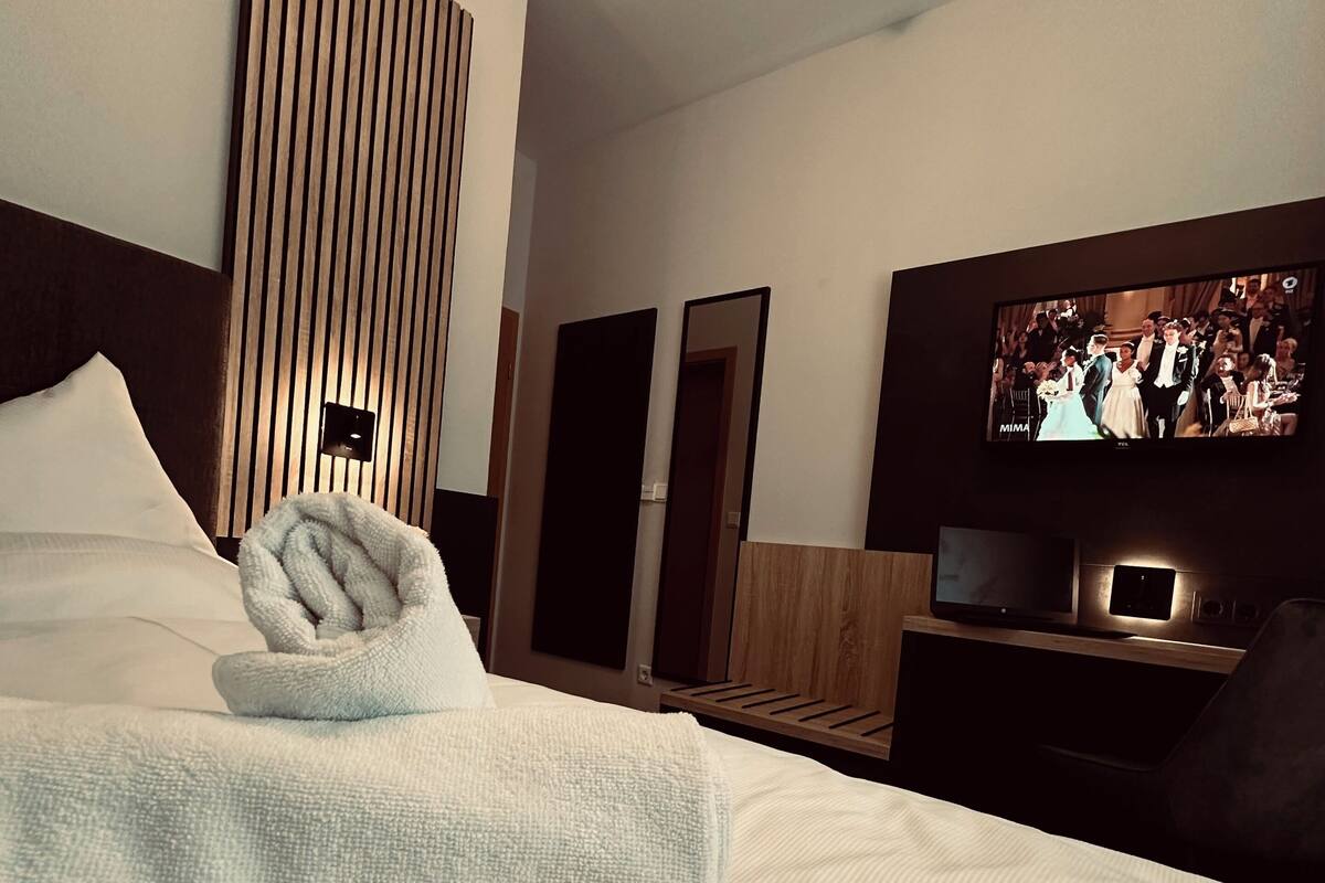 A hotel room with a neatly made bed, a television on a wooden stand, and a wall-mounted mirror.