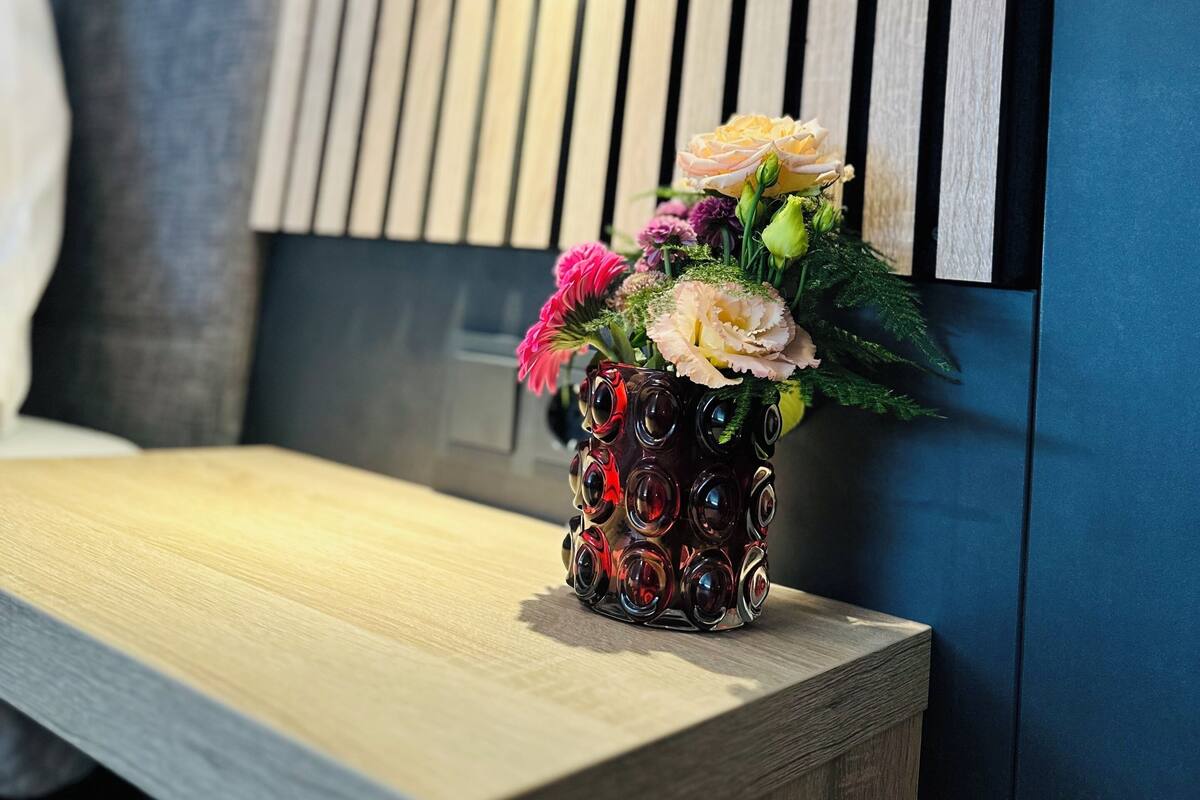 A wooden bench with a vase of flowers in front of a wall with vertical wooden slats and a small picture frame.