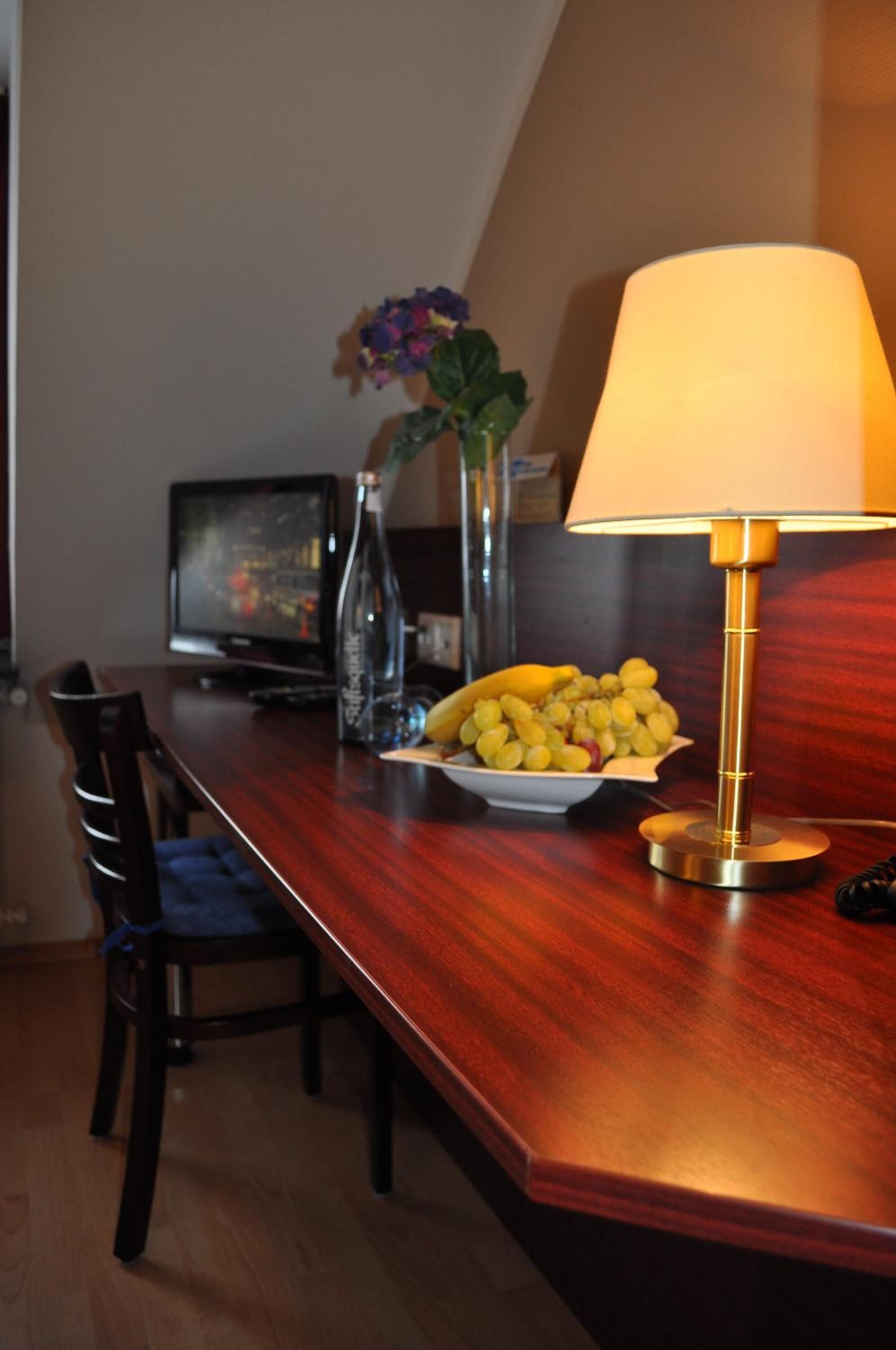 Une table à manger en bois, sur laquelle se trouvent un saladier de fruits, une bouteille et un vase rempli de fleurs.