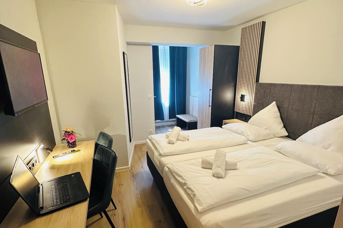 A hotel room with a bed, a desk with a laptop, a chair, and a TV.