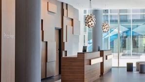 A modern reception area with a wooden reception desk, geometric wall panels, and a large glass window offering a view of the outdoors.