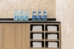 Un mueble de madera con encimera negra. Sobre la encimera, seis botellas de agua y seis toallas blancas dobladas con pulcritud.