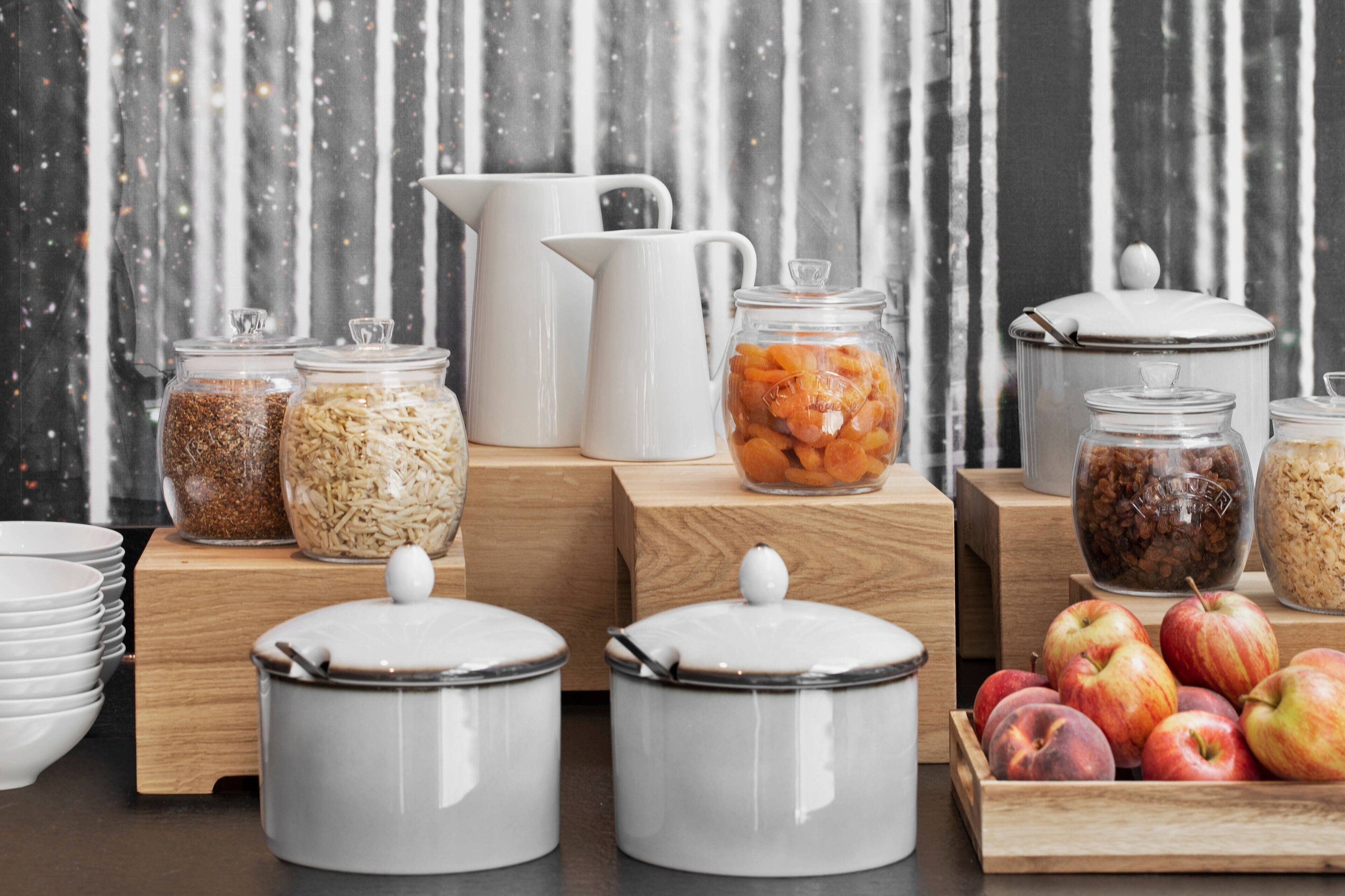 A kitchen counter with various food storage containers, a coffee maker, and a wooden cutting board with apples.