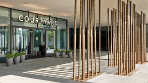 A Courtyard by Marriott hotel entrance with a modern design, featuring tall decorative columns and potted plants.