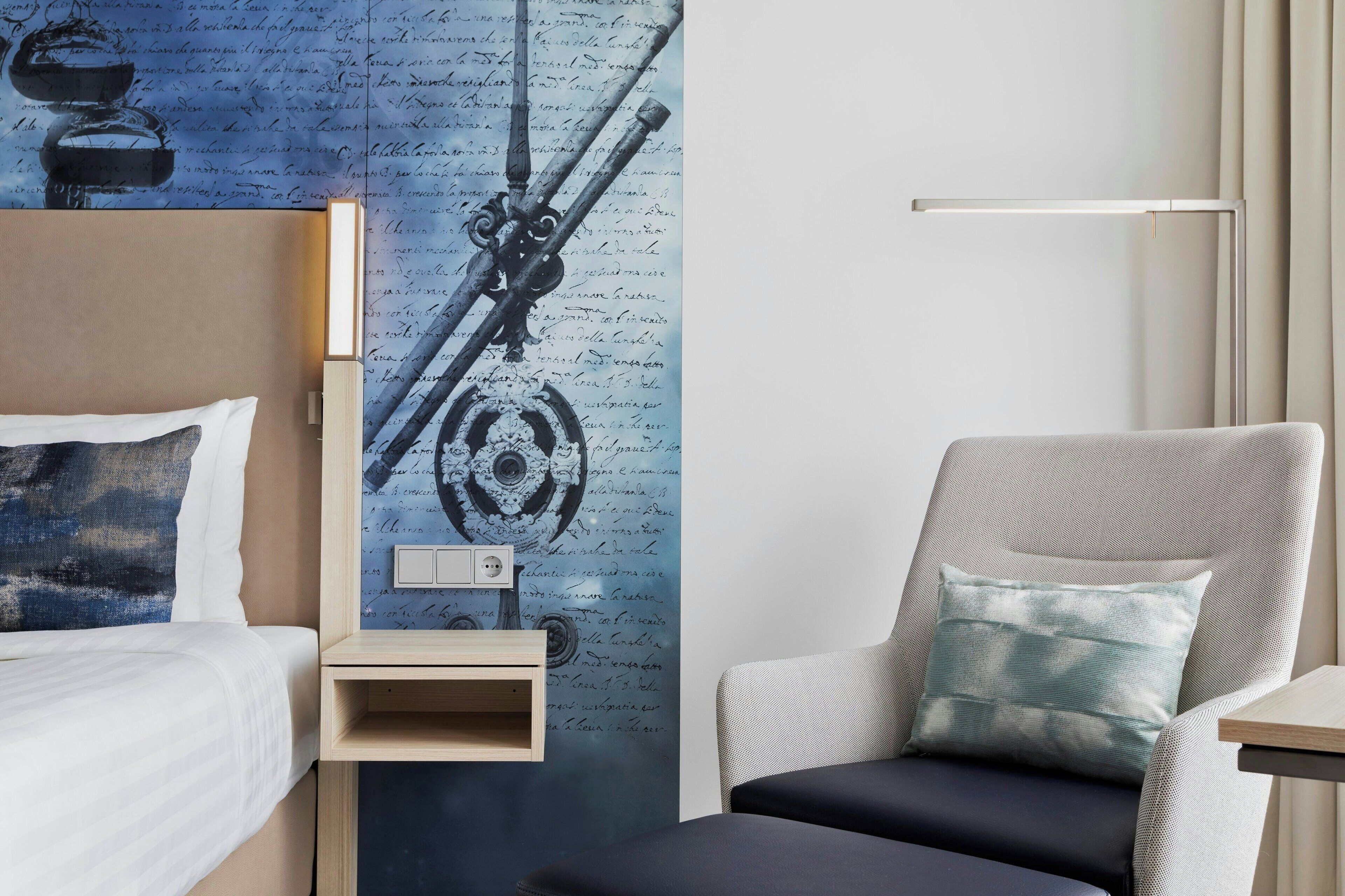 Habitación de hotel con una cama, una silla, una mesita de noche y una pared con un diseño decorativo.