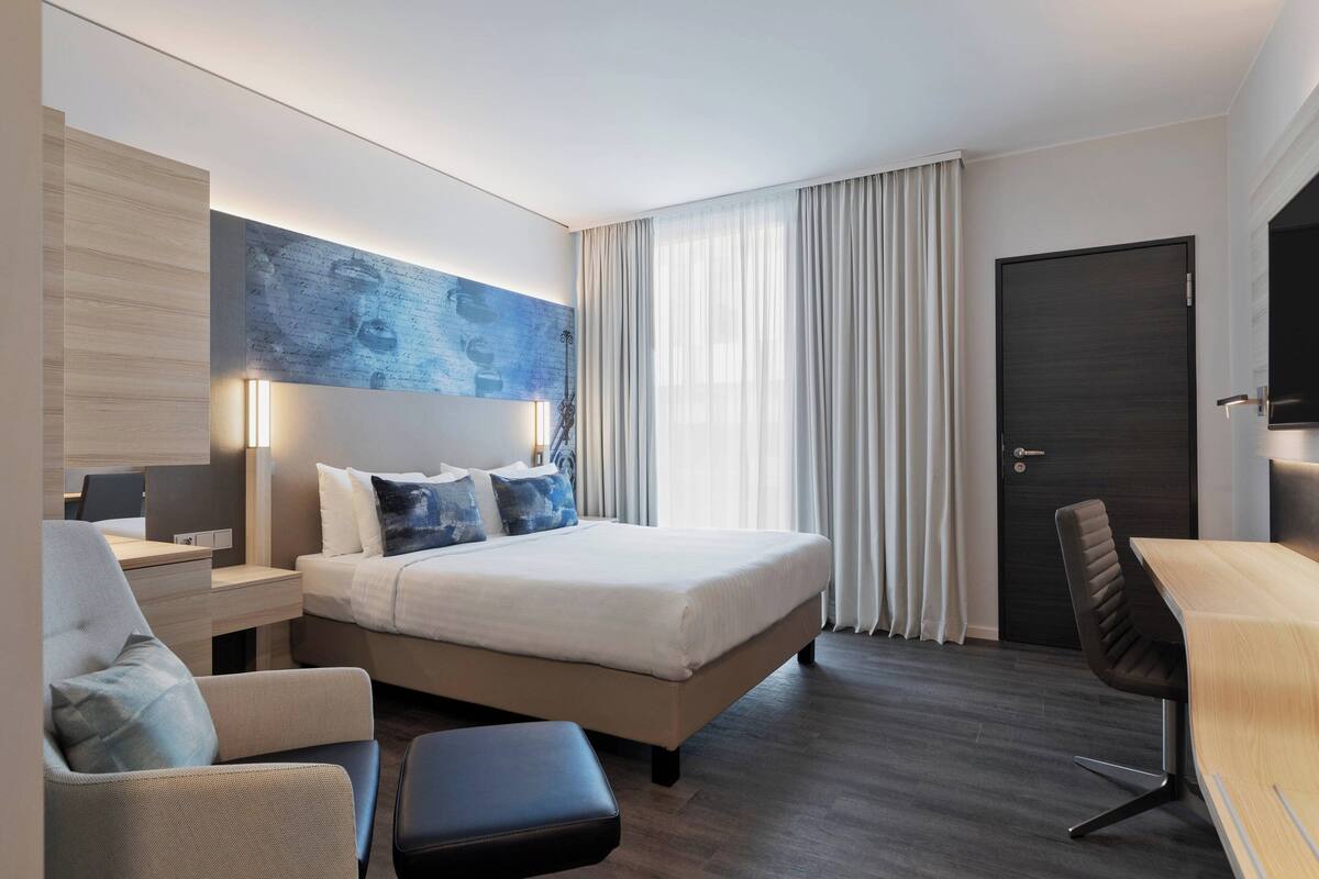 A modern hotel room with a large bed, a desk, a chair, and a television.