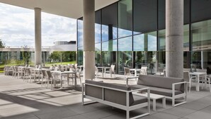 An outdoor seating area with tables and chairs, large windows, and a modern architectural design.