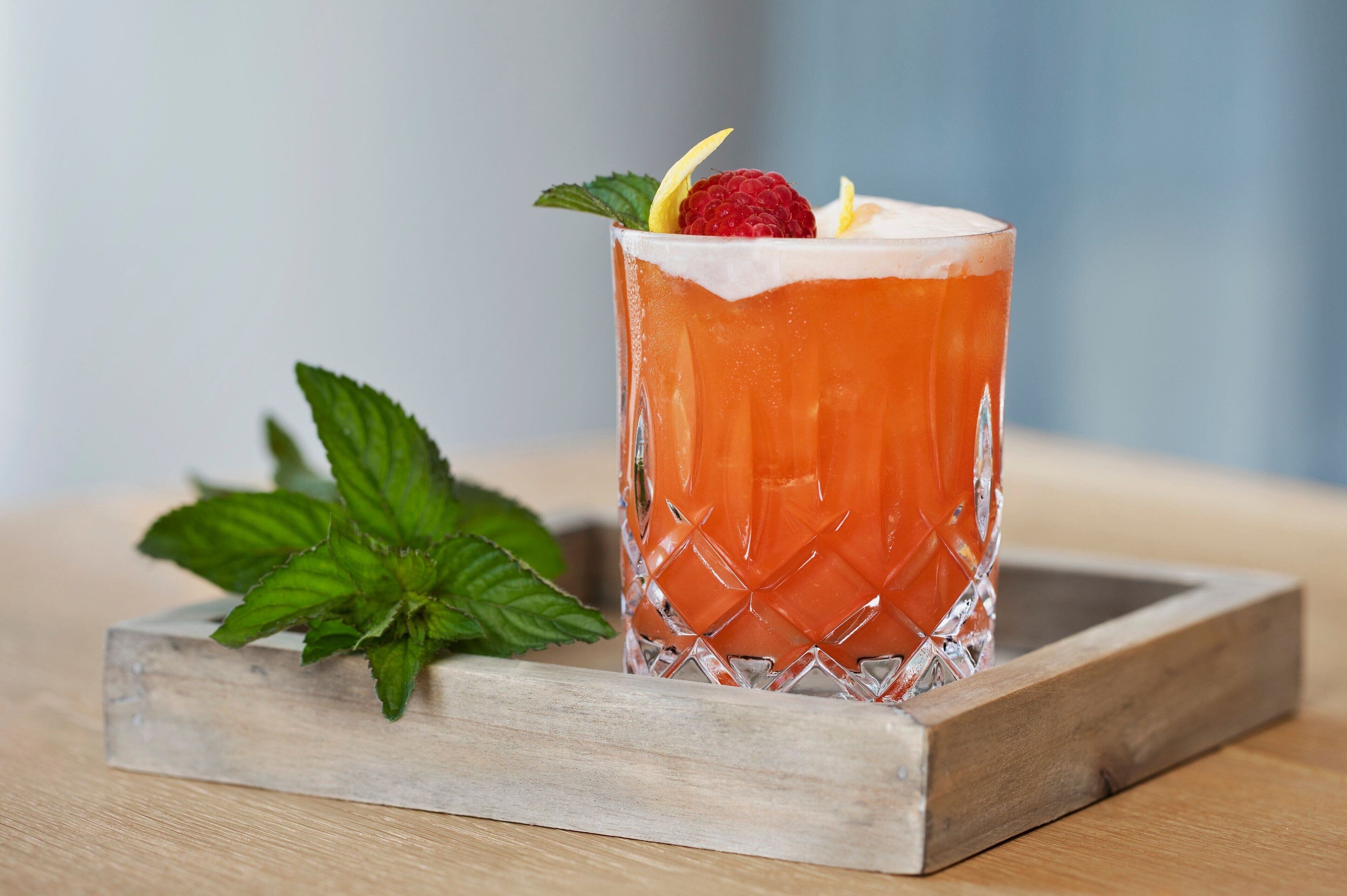 A cocktail glass with a raspberry garnish on a wooden tray.