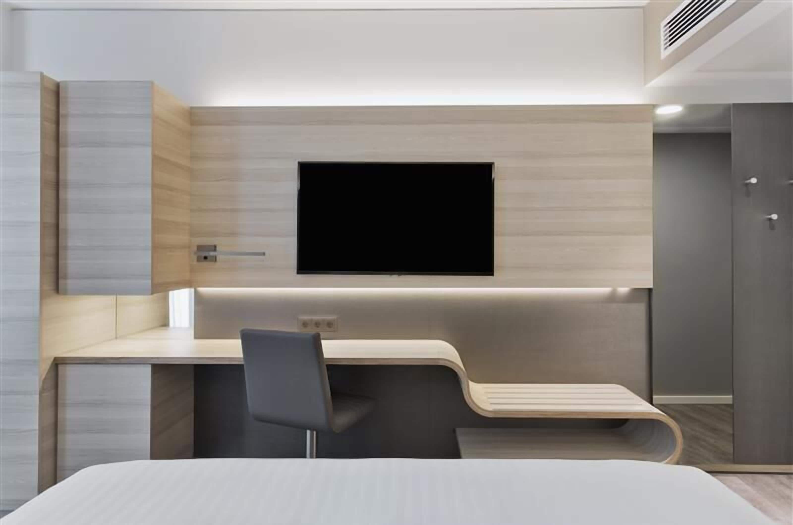 Une chambre d’hôtel moderne équipée d’un téléviseur à écran plat fixé au mur, d’un bureau avec une chaise et d’un lit.