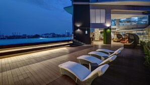 Een terras op het dak met ligbedden, een zwembad en uitzicht over de stad.
