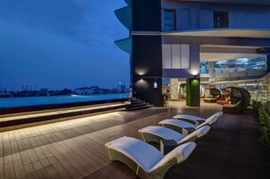 A rooftop lounge area with sun loungers, a pool, and a city view.