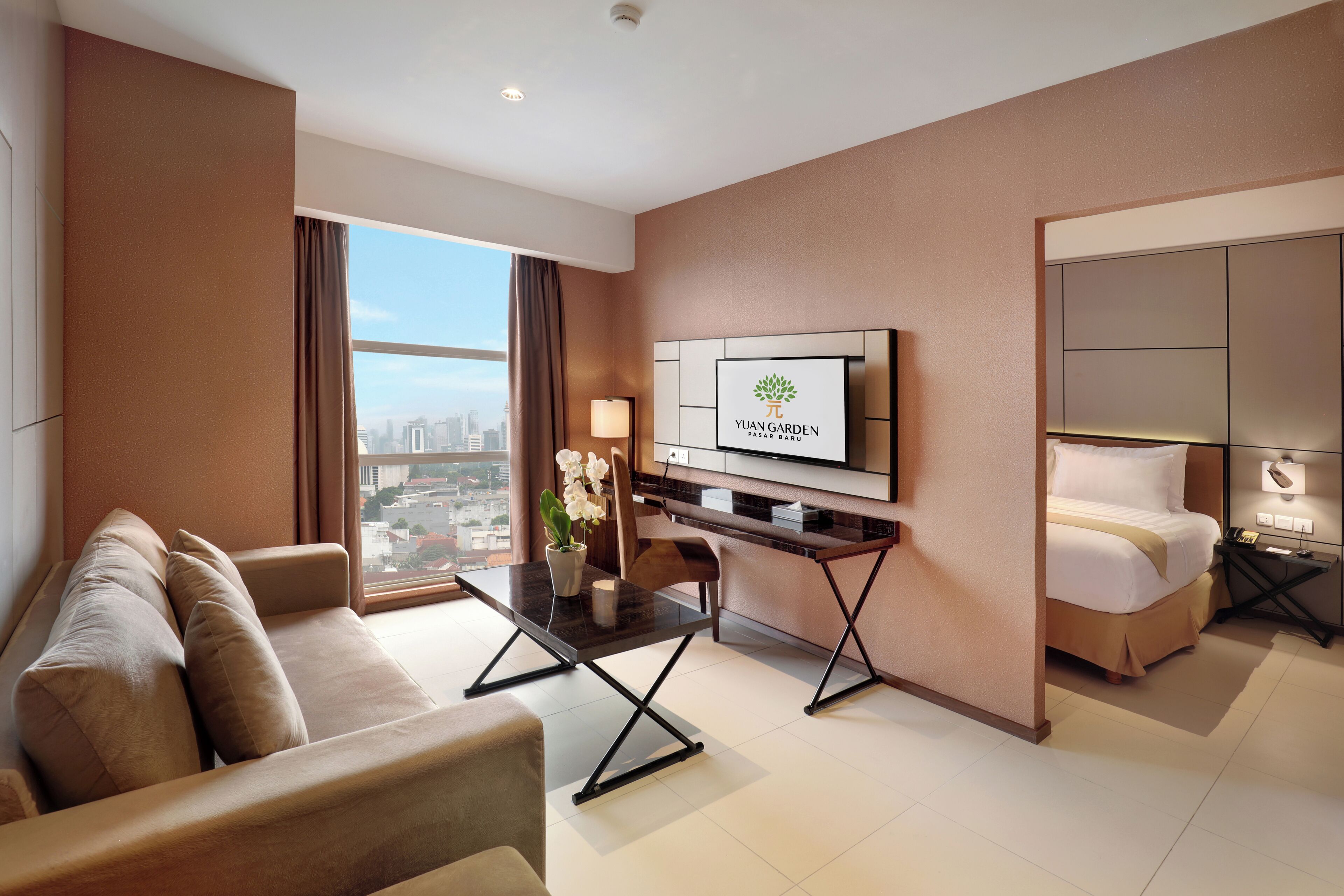 A modern hotel room with a sofa, a dining table, a TV, and a bed.