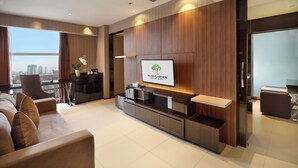 Een moderne hotellobby met een groot televisiescherm waarop de naam van het hotel staat, een bank, een bijzettafeltje en een stadszicht door grote ramen.