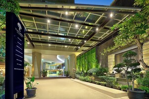 A hotel lobby with a glass ceiling, potted plants, and a sign listing amenities like rooms, a restaurant, and a wellness center.