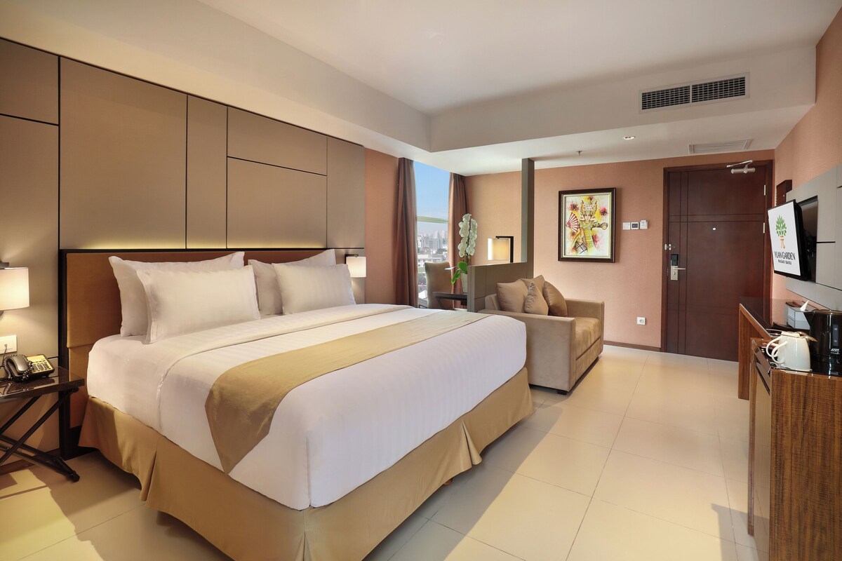 A hotel room with a large bed, a sofa, a TV, and a desk with a phone.
