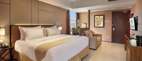 A hotel room with a large bed, a sofa, a TV, and a desk with a phone.