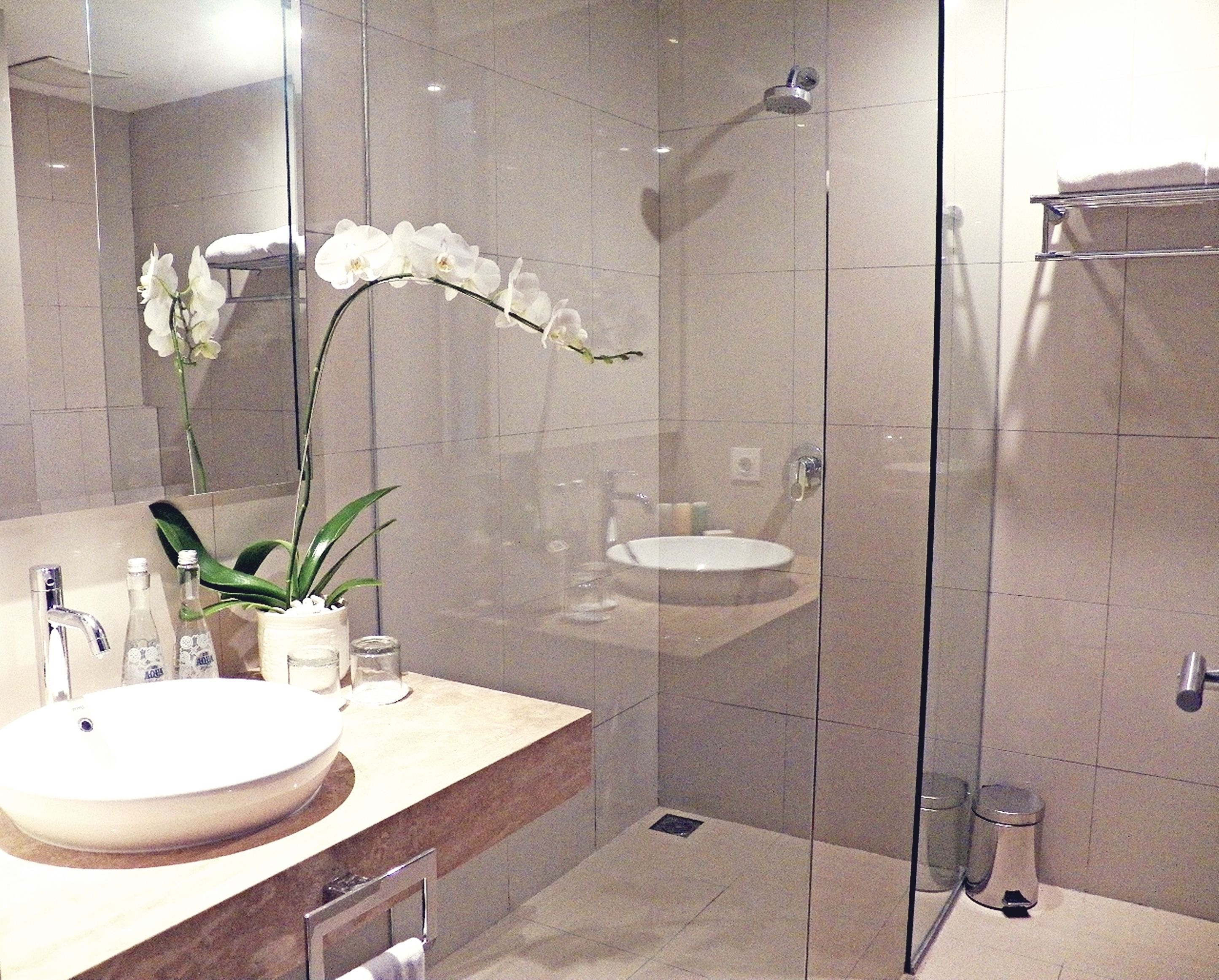 A modern bathroom with a glass shower enclosure, a sink, and a vase with white orchids.