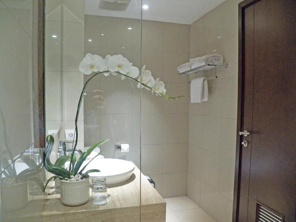 Ein modernes Badezimmer mit Duschkabine aus Glas, einer weißen Orchidee, einem Waschbecken mit Spiegel und einem Handtuchhalter.