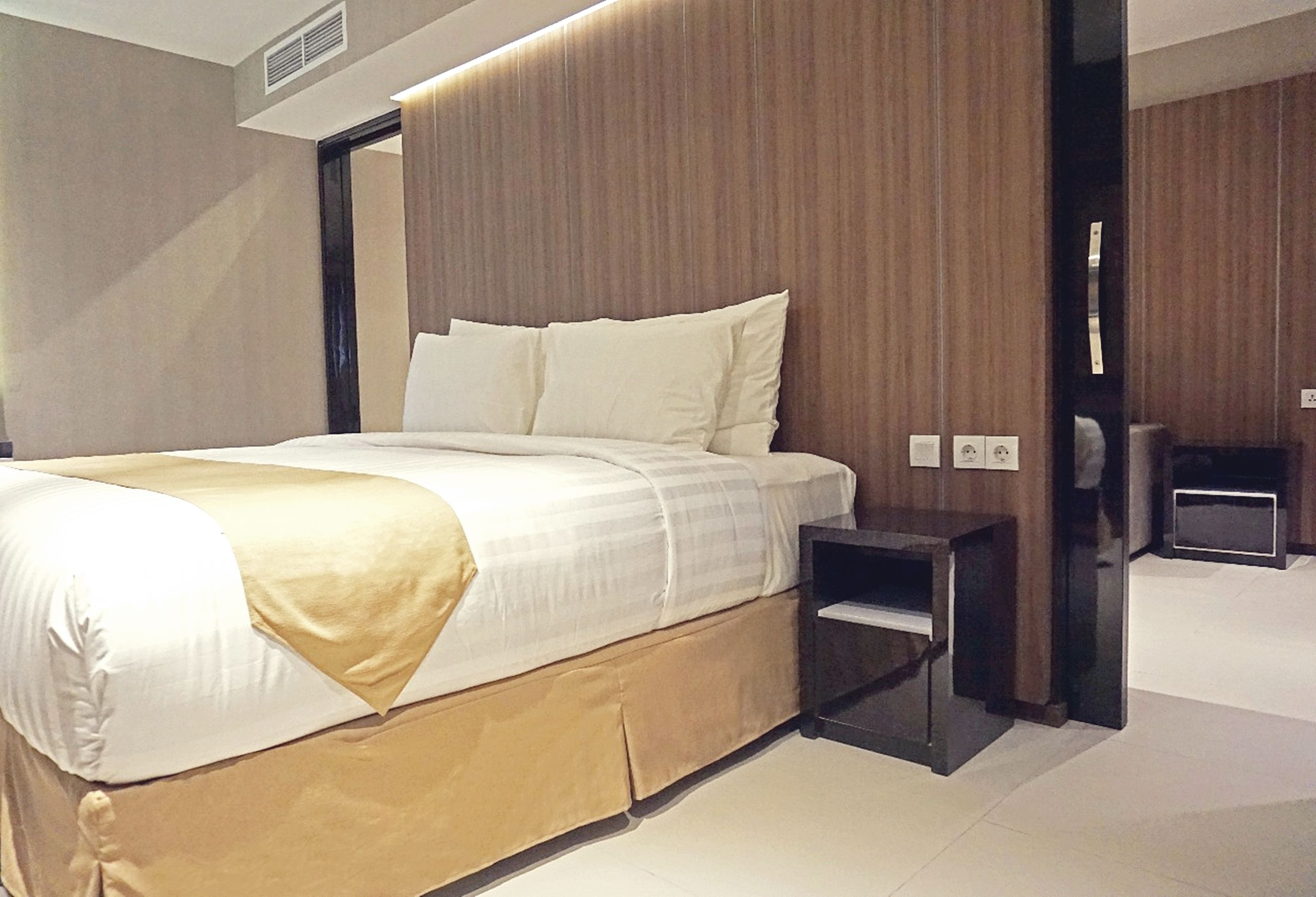 A modern hotel room with a large bed, a wooden headboard, and a small bedside table.
