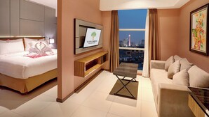 Een hotelkamer met een bed, een slaapbank, een televisie en uitzicht op de stad.