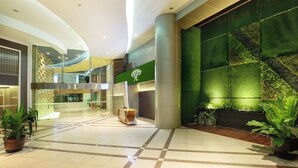 Een ruime lobby met een groene wand, een receptiebalie en potplanten.