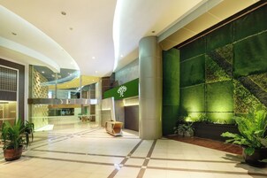 A spacious lobby with a green wall, a reception desk, and potted plants.
