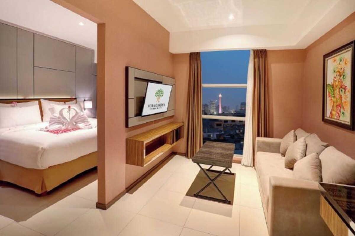 Een moderne hotelkamer met een bed, een televisie, een bank en uitzicht op een stadsgezicht.