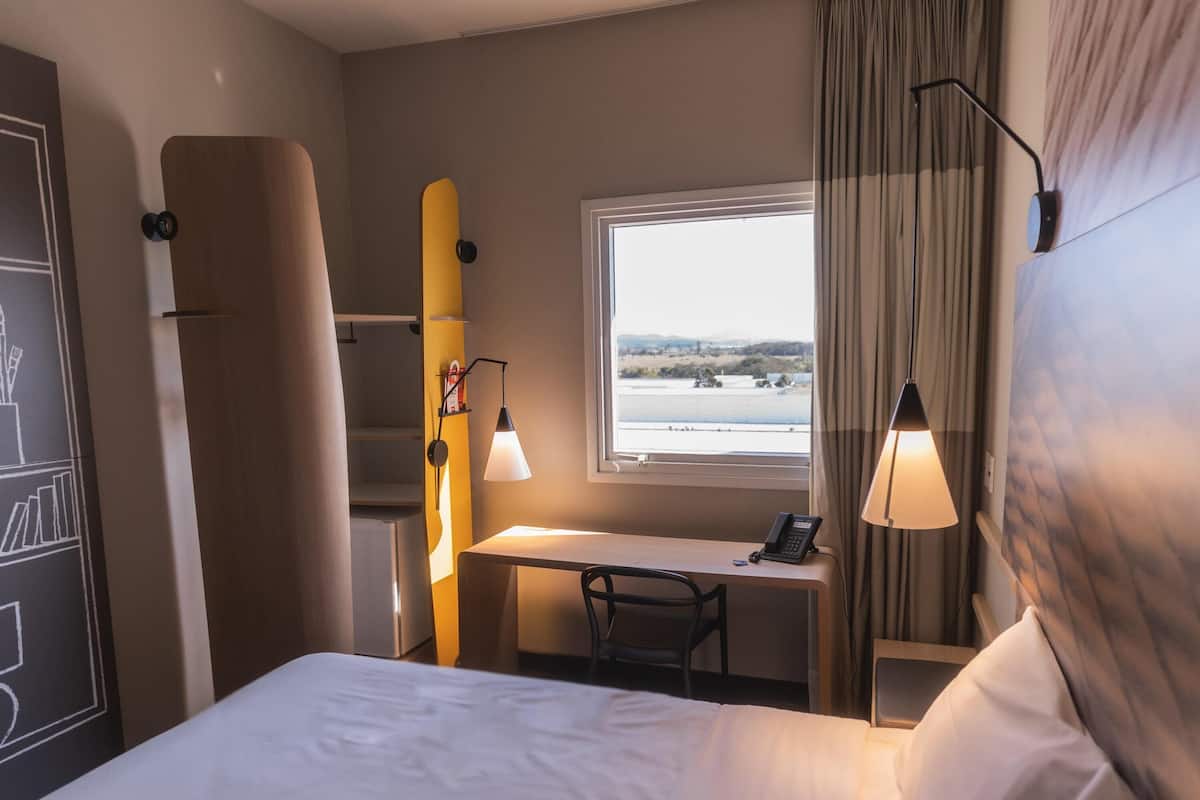 A hotel room with a bed, desk, chair, and a window with a view of a landscape.