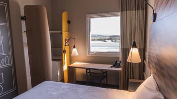 Et hotelværelse med seng, skrivebord, stol og et vindue med udsigt over landskabet.