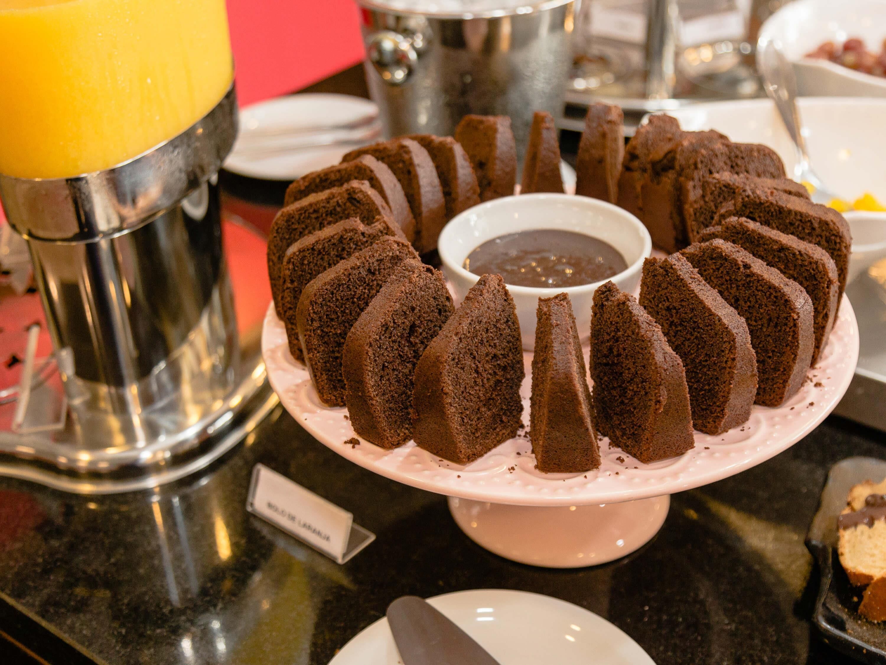 A cake stand with a bundt cake and a small bowl of chocolate sauce.