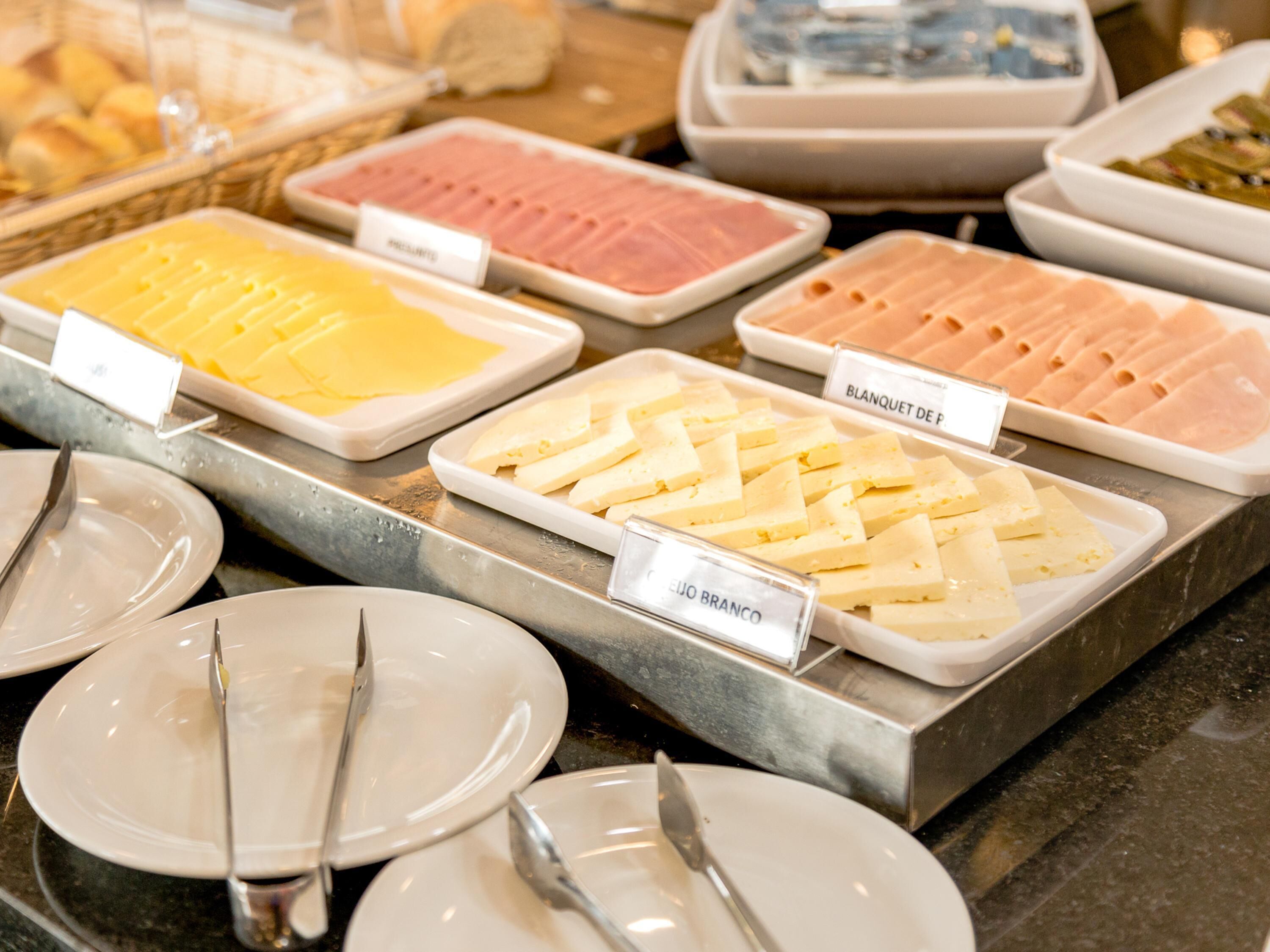 Un bufé con diversas opciones de comida, incluyendo queso, jamón y otras preparaciones frías.
