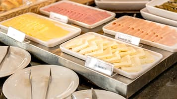 Un bufé con diversas opciones de comida, incluyendo queso, jamón y otras preparaciones frías.