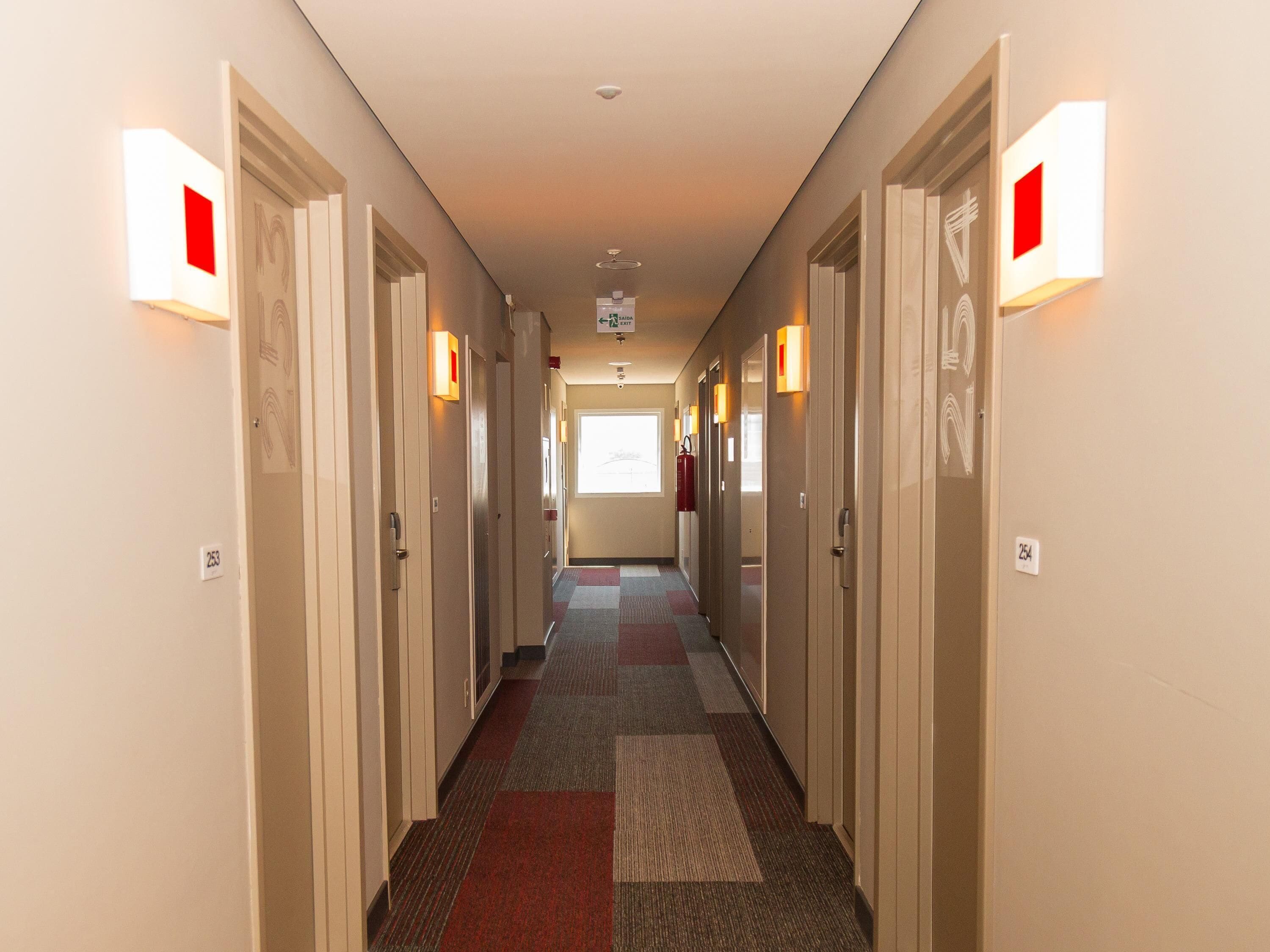 A hotel hallway with carpeted floors, doors with numbers, and wall-mounted light fixtures.