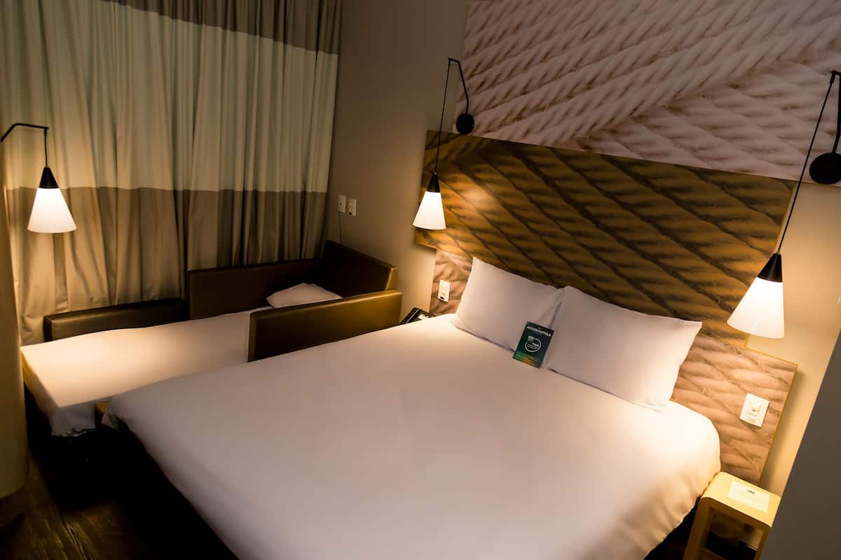 A hotel room with a large bed, two bedside tables, a nightstand, and a headboard with a patterned design.