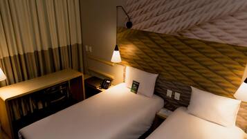 A hotel room with two beds, a desk, a telephone, and a wall-mounted lamp.