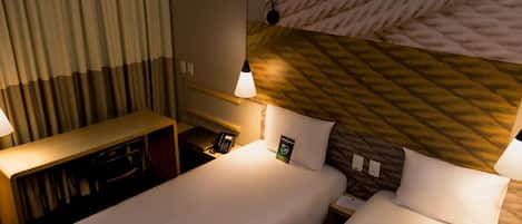 Una habitación de hotel con dos camas, un escritorio, un teléfono y una lámpara en la pared.