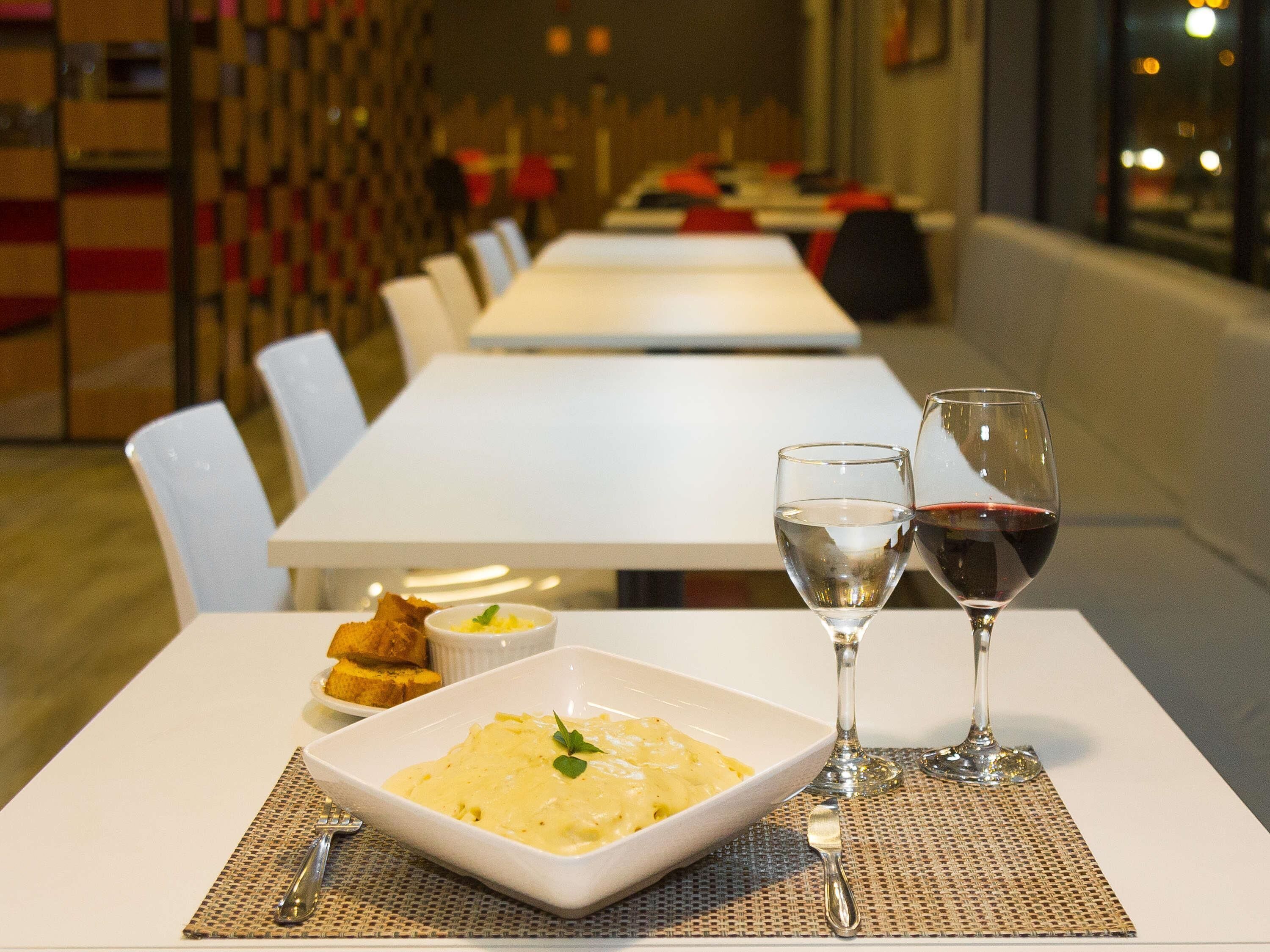 A dining table with a plate of food, two wine glasses, and a small bowl of sauce.