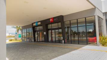 A modern building with a glass facade, a prominent 'ibis' sign, and a paved entrance area.