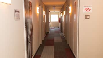 Um corredor de hotel com pisos revestidos de carpete, portas em ambos os lados e um extintor de incêndio fixado na parede.
