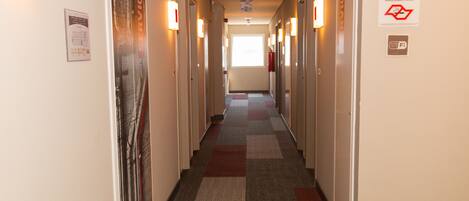 Pasillo de hotel con pisos alfombrados, puertas a ambos lados y un extintor colgado en la pared.