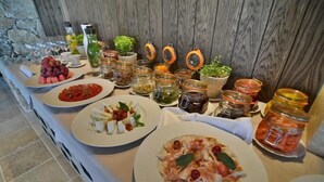 A buffet table with various dishes, including pasta, salads, and fruits, along with several jars of pickles and condiments. - Zornitza Family Estate (Zornitza)