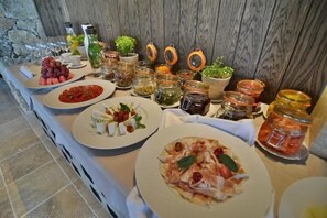 A buffet table with various dishes, including pasta, salads, and fruits, along with several jars of pickles and condiments. - Zornitza Family Estate (Zornitza)