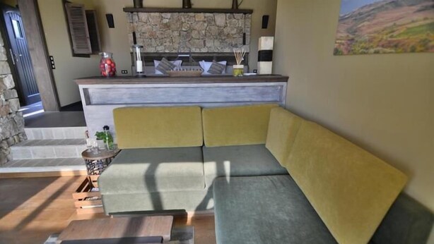 A modern living room with a sectional sofa, a stone fireplace, and a kitchen area with a stone backsplash. - Zornitza Family Estate (Zornitza)
