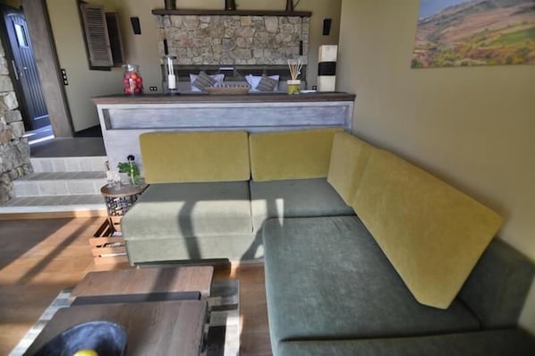A modern living room with a sectional sofa, a stone fireplace, and a kitchen area with a stone backsplash. - Zornitza Family Estate (Zornitza)