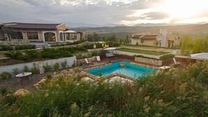 A pool area with a stone border, lounge chairs, and a view of mountains in the background. - Zornitza Family Estate (Zornitza)